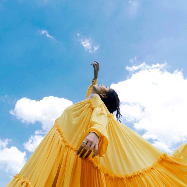 woman wearing yellow long-sleeved dress under white clouds and blue sky during daytime